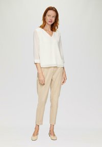Blouse blanche à col en V avec des manches trois-quarts en tissu transparent, associée à un pantalon beige clair sur mesure et des ballerines beiges, design minimaliste.