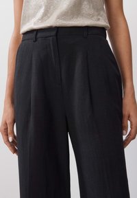 Mustat taitetut housut kevyestä kankaasta, joissa on sileä pinta, suora lahje ja etutaskut.