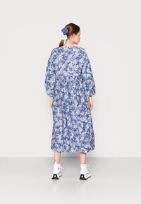 Vestido midi floral com padrões azuis e brancos, mangas longas, cintura elástica e um corte solto. Combinado com botas de tornozelo brancas.