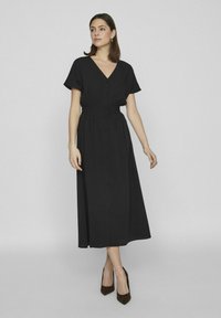 Čierne midi šaty s V-výstrihom, krátkymi rukávmi a gombíkovým zapínaním vpredu. Vyrobené z mäkkej tkaniny, majú vytiahnutý pás a splývavú sukňu.