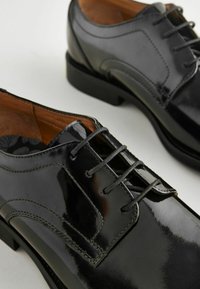 Schwarze Lederschuhe mit glänzender Oberfläche, Schnürdesign und dezentem dekorativem Stich. Sie haben eine glatte Textur und einen niedrigen Absatz.