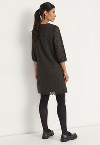 Musta vihreä pitsimekko, jossa on kolme neljännestä puffihihasta ja aaltoileva helma, sekä mustat sukkahousut ja mustat kengät. Rakenteellinen, kevyt kangas.