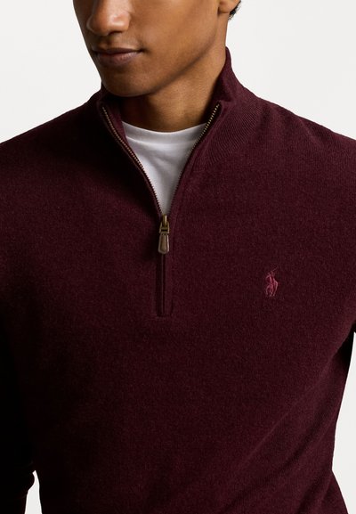 Pull en bourgogne foncé avec un col zippé demi-long. Fabriqué en tissu texturé avec un petit logo sur la poitrine. Accentué par une fermeture éclair dorée.