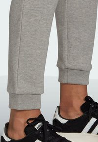 Grå bomullsträningsbyxor med avsmalnande benslut, tillsammans med svarta sneakers med vita ränder och detaljerade snören. Mjuk textur, figurnära form.