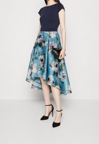 Blommig midi-klänning med en navy-färgad figurnära bodice och hög-låg fåll. Utrustad med blått tyg med stora blommor. Avslutad med svarta ankelsandaler.