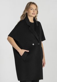 Czarny wełniany płaszcz z kołnierzem, krótkimi rękawami, dwoma przednimi kieszeniami i dwoma guzikami. Gładka faktura z dopasowaną sylwetką.