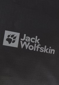 Czarna tkanina z srebrnym logo w kształcie odcisku łapy oraz napisem "Jack Wolfskin" w wyróżniającym się, nowoczesnym kroju pisma.