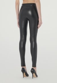 Zwarte faux leren leggings met een hoge tailleband, een gladde textuur en een strakke pasvorm, gecombineerd met zwarte hoge hakken.