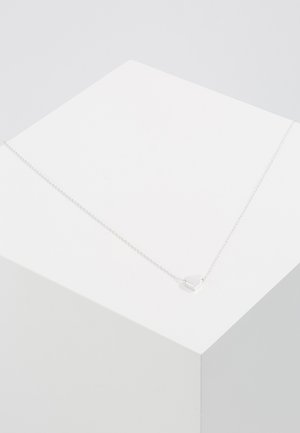 Collier en chaîne argentée avec un pendentif en forme de cœur au fini poli, exposé sur un piédestal blanc. Design simple, épaisseur moyenne.