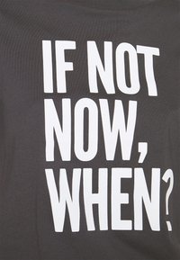 Camiseta de algodón gris con texto en blanco en negrita que dice: "¿SI NO AHORA, CUÁNDO?" El diseño es sencillo, con un corte relajado y un cuello redondo.