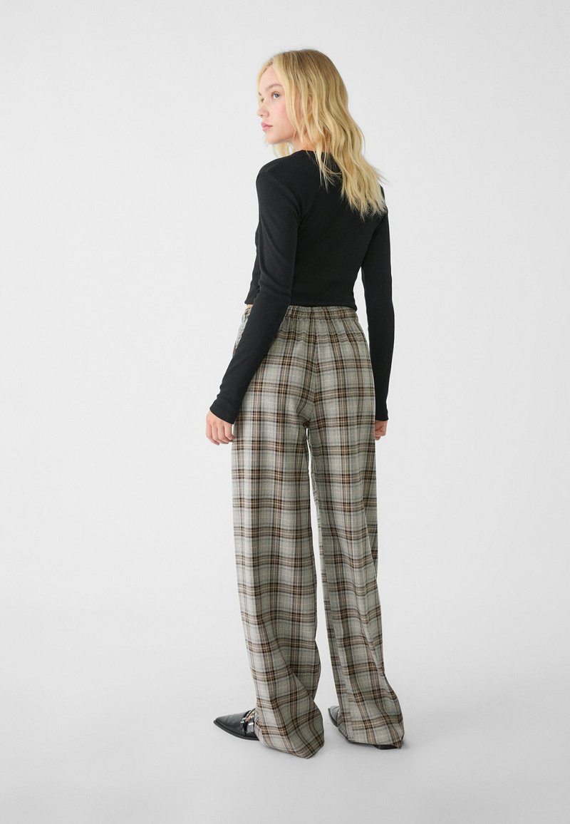 Schwarzes Langarmoberteil und graue karierte weite Hose mit braunen Akzenten. Das Outfit verfügt über einen elastischen Bund und eine glatte Stofftextur.