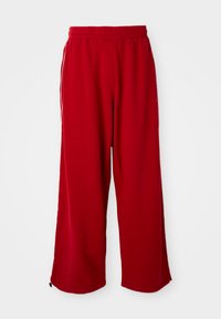 Pantaloni larghi rossi realizzati in tessuto morbido con vita elastica e strisce laterali bianche. Presentano una texture pulita e liscia.