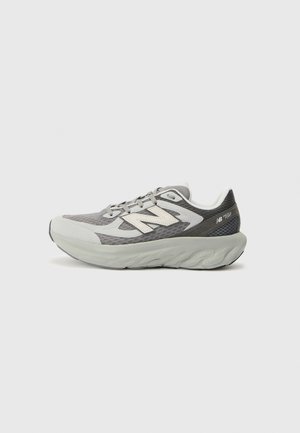 Grå og hvid New Balance løbesko med tyk polstret sål og mesh overdel, vist fra siden på ensfarvet lys baggrund.