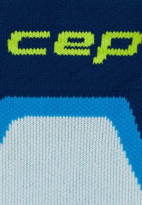 Primo piano di un tessuto a maglia blu navy con il testo "cep" di colore verde brillante e un motivo circolare bianco e blu sottostante.