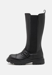 Bottes noires montantes en cuir lisse avec des panneaux latéraux élastiques, une bride avant avec boucle en métal et une semelle épaisse et robuste.