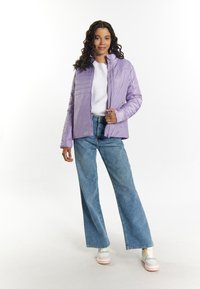 Lichtpurper pufferjack met een ritsluiting, gecombineerd met een witte trui en wijde blauwe jeans. Het model draagt multikleuren sneakers.
