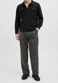 Zwarte button-up shirt met twee borstzakken, gedragen over een wit shirt. Combineren met grijze geplaatste broeken en zwarte stevige schoenen.