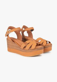 Sandalias de cuña con un upper de imitación de piel de naranja texturizada, tiras entrelazadas y una suela de plataforma de color marrón claro en capas. Correa en el tobillo ajustable.