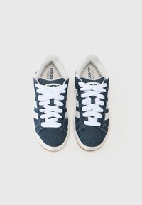 Zapatillas de denim azul con cordones blancos, presentan tres rayas blancas a los lados, puntera redondeada y tela texturizada. Suela de goma.