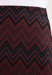Tissu noir avec un motif en zigzag rouge et bleu, surface texturée et léger éclat. Conception de taille standard.