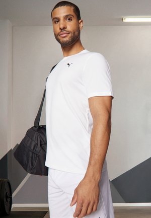 Wit sportshirt met zwarte branding, gecombineerd met witte shorts. De persoon draagt een donkergrijze sporttas. Eenvoudig ontwerp, gladde textuur.