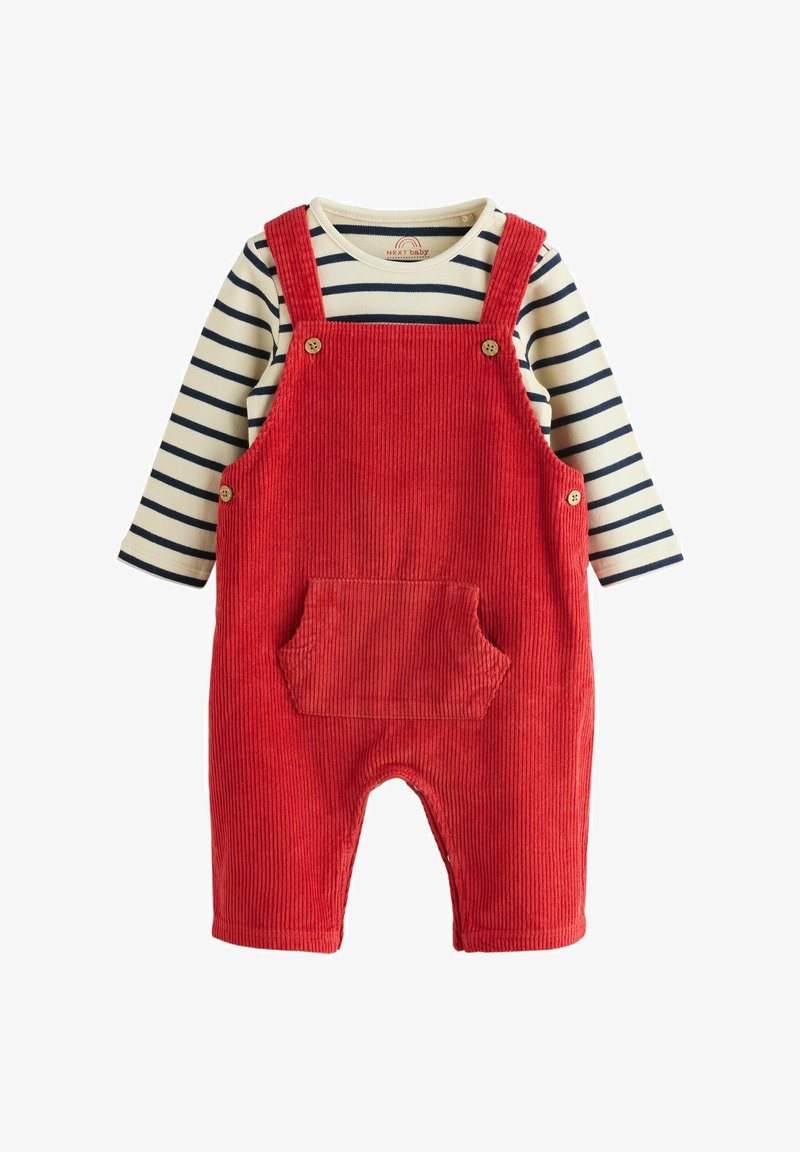 Czerwone ogrodniczki dla niemowląt z korduroy z przednią kieszenią, noszone na kremowej i granatowej koszulce z długim rękawem w paski.