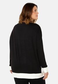 Long-sleeve top in black with a white cuff and hem. Features a relaxed fit with a rounded back neckline and smooth fabric texture.