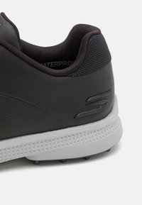 Black waterproof sneaker with textured leather upper, padded collar, and gray rubber sole featuring a raised logo detail on the side.