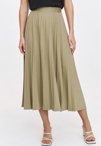 Plisowana spódnica midi w oliwkowym kolorze, charakteryzująca się wysokim stanem i zwiewną teksturą. Połączona z jasnymi, paseczkowymi obcasami w bloku.
