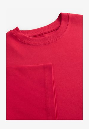 Sweatshirt en coton rouge avec un col rond côtelé et des coutures visibles. Il dispose d'une grande poche avant, d'une texture douce et d'une coupe décontractée.