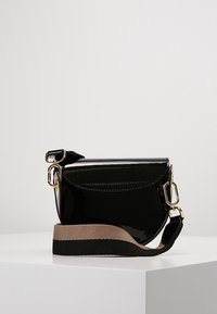 Černá lesklá kožená crossbody taška s zakřiveným designem, zlatými detaily a texturovaným popruhem se černými a béžovými pruhy.