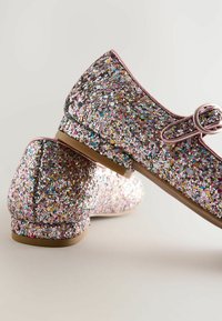 Glittrande skor med rundade tår och rosa detaljer. Den glittriga ytan har olika färger och är placerad på en låg, brun sula.