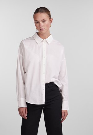 Hvit skjorte med krage, lange ermer og avslappet passform. Kombinert med svarte bukser, stoffet ser litt teksturert ut.