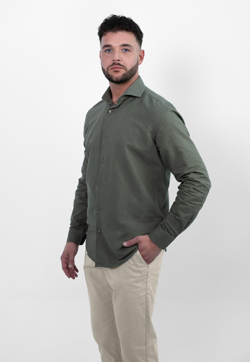 Olijfgroen overhemd met knopen, lange mouwen en een slim fit, gecombineerd met lichtbeige broek. Zachte textuur; subtiele glans.