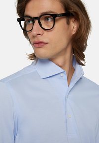 Svetlo modra polo majica s kratkimi rokavi in gumbasto ovratnikom, mehka tekstura tkanine, ozek kroj in subtilni šivi.