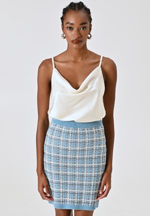 Top in satin bianco con scollo a cowl e spalline sottili, abbinato a una gonna aderente a maglia a quadri blu e bianchi con vita e orlo a costine.
