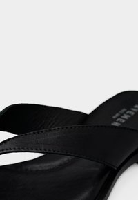 Μαύρο δερμάτινο σαγιονάρι με δύο επικαλυπτόμενα λουριά και υφή στην σόλα. Διαθέτει λείο φινίρισμα και διακριτικές ραφές ως διακοσμητικά στοιχεία.