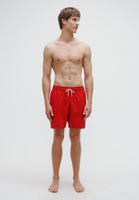 Calções de banho vermelhos com cintura ajustável por cordão, feitos de tecido leve. Apresentam um corte descontraído e bainha que termina acima do joelho.