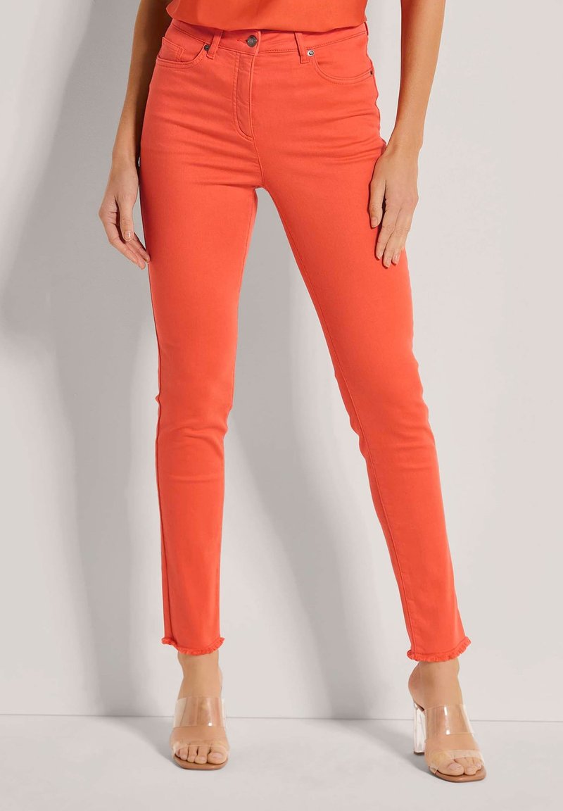 Leuchtend orangefarbene High-Waist-Jeans mit slim fit, ausgefransten Knöcheln und fünf Taschen-Design, kombiniert mit klaren Blockabsatzsandalen.