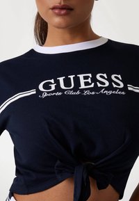 Navy blue cropped t-shirt with white collar and branding. Features a knotted detail at the hem. Made from soft cotton material.