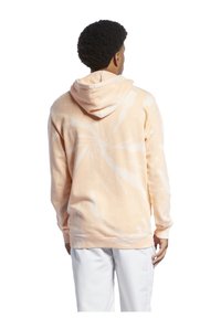 Haut à capuche tie-dye pêche avec un col à cordon, manches longues et poignets côtelés. Le tissu semble doux et décontracté dans son design.