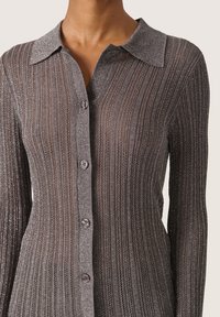 Camisa gris de botones con patrón de estrías verticales, que presenta un cuello, un ligero brillo y hilos metálicos. Los botones son oscuros y redondos.