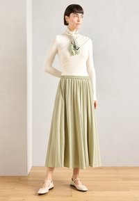 Lys beige langermet topp, plissert, gulvlengde salvieskjørt og kremfargede leilisko. Skjerf med blomstermønster.