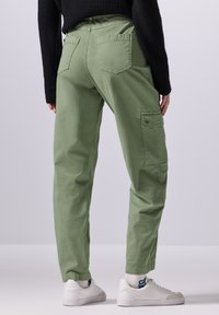 Grønne bomulds cargo bukser med en tapered design, sidelommer og en baglomge. Paret med hvide sneakers og en struktureret sort sweater.