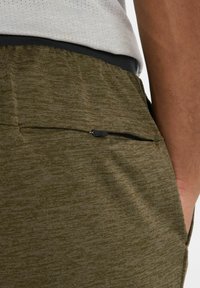 Oliivinvihreät urheilushortsit, joissa on teksturoitu kuvio, varustettuna vetoketjullisella taskulla oikealla puolella ja joustavamalla vyötäröhihnalla.