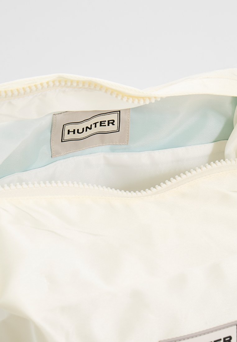 Interior de bolsa de tela blanca con un forro azul claro. Cierre de cremallera en la parte superior y una prominente etiqueta de "HUNTER" en el interior. Textura suave.