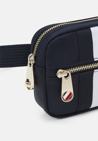 Borsa a tracolla in nylon blu navy con cerniere dorate, caratterizzata da un design a righe e un dettaglio circolare in rosso, bianco e nero.