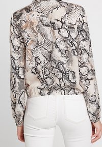 Persona che indossa un top a maniche lunghe con stampa di serpente beige e nera abbinato a jeans bianchi a vita alta, visto da dietro.