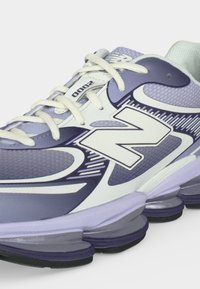 Ανοιχτό μωβ και λευκό αθλητικό παπούτσι New Balance 2000 με μαξιλαρωμένη σόλα, λευκά κορδόνια και μεγάλο λογότυπο "N" στο πλάι.