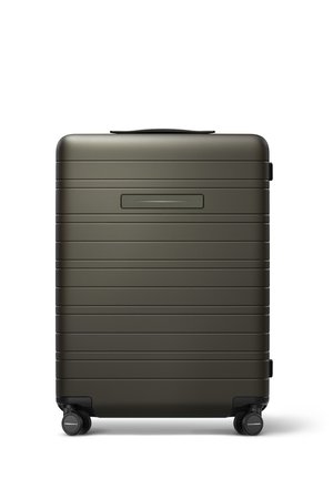 Valise rigide de couleur vert foncé, présentant une surface texturée avec des rainures horizontales, une poignée supérieure et quatre roues noires pour la mobilité.